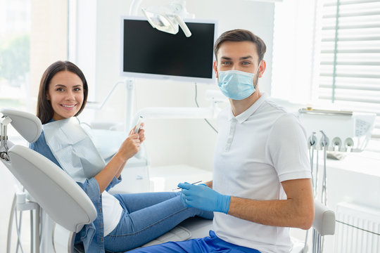 side view of male dentist in mask with parient sittting in dental chair looking at the camera