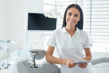 cheerful dentist in coat using tablet in office and looking at the camera