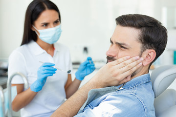 side view of caucasian client touching face while having toothache near dentist in the hospital