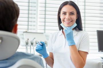 female dentist at procedure holding dental drill in modern dental clinic and looking at the camera