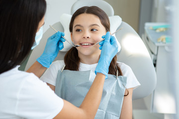 dentist examining teeth of smiling client in dental chair