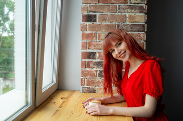 Girl drinks coffee on a wooden table near a brick column
