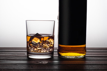Whiskey in a glass with ice and next to a bottle of whiskey on a wooden background