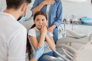 small client with dentist and pain in the teeth sitting in dental chair while mother standing near...