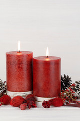 Burning red Christmas candles on a rustic white wooden background with natural potpourri elements and pine cones. Vertical photo