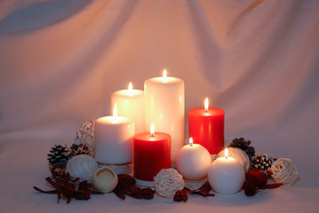 Burning red and white Christmas candles surrounded by natural potpourri and pine cones on a draped...
