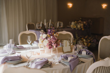 Coziness and style. Modern event design. Table setting at wedding reception. Floral compositions with beautiful flowers and greenery, candles, laying and plates on decorated table.