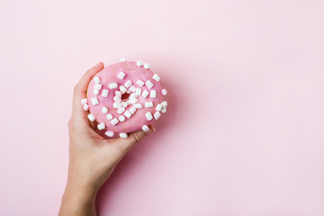 Female hand holding pink donut with marshmallows over pink background
