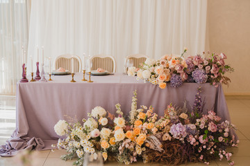 Coziness and style. Modern event design. Table setting at wedding reception. Floral compositions with beautiful flowers and greenery, candles, laying and plates on decorated table.