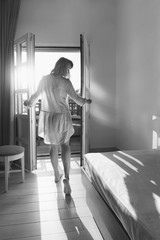 Beautiful young woman standing in doorway at sunset. Back view of sensual lady looking at sunny sky at daytime. Pretty girl enjoying morning sunlight. Female figure at door entrance in sunlit room