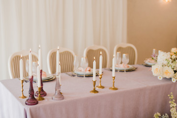 Coziness and style. Modern event design. Table setting at wedding reception. Floral compositions with beautiful flowers and greenery, candles, laying and plates on decorated table.