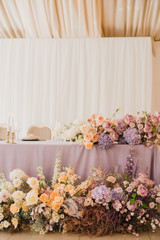 Coziness and style. Modern event design. Table setting at wedding reception. Floral compositions with beautiful flowers and greenery, candles, laying and plates on decorated table.