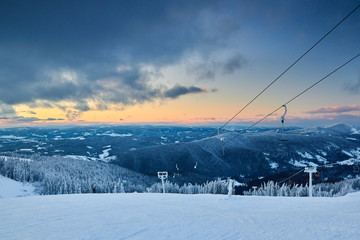 Evening winter landscape in the mountains with fir tree forest on sunset. Snow covered hills after...