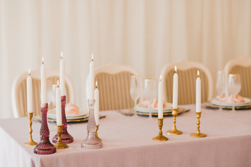 Coziness and style. Modern event design. Table setting at wedding reception. Floral compositions with beautiful flowers and greenery, candles, laying and plates on decorated table.