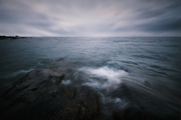 Long exposure and waves hitting the rocks in the foreground bad weather and horizon with rocks in the background
