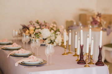 Coziness and style. Modern event design. Table setting at wedding reception. Floral compositions with beautiful flowers and greenery, candles, laying and plates on decorated table.
