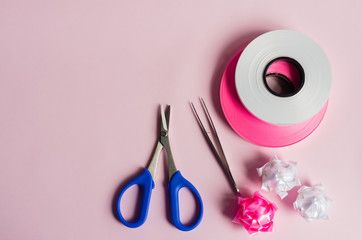 Ribbon roll on pink background with scissor and ..tweezers