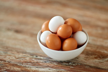 food, culinary and cooking concept - close up of natural chicken eggs in ceramic bowl on wooden table