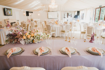 Coziness and style. Modern event design. Table setting at wedding reception. Floral compositions with beautiful flowers and greenery, candles, laying and plates on decorated table.