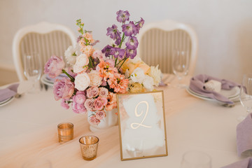 Coziness and style. Modern event design. Table setting at wedding reception. Floral compositions with beautiful flowers and greenery, candles, laying and plates on decorated table.