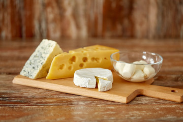 food and eating concept - different kinds of cheese on wooden cutting board