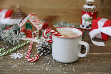 Obraz na płótnie Canvas Close-up christmas composition with gingerbread house, mug of cocoa, caramel canes gingerbread house and decorations on wooden background with copy space for text. 