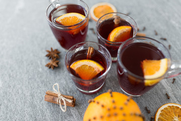 christmas and seasonal drinks concept - glasses of hot mulled wine with orange and cinnamon on grey...