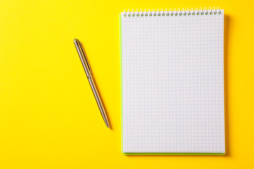 the white open notepad on silver pen isolated on the yellow background