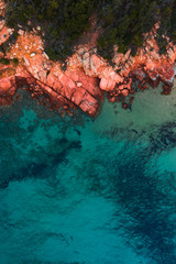 A top-down drone view of the amazingly calm, clear water and red rocks on the island of Sardinia in...