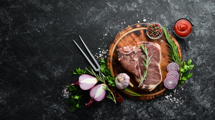 Raw T-bone steak on a black stone table. Top view. Free space for your text.