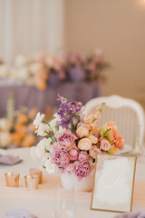 Coziness and style. Modern event design. Table setting at wedding reception. Floral compositions with beautiful flowers and greenery, candles, laying and plates on decorated table.