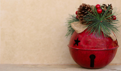 large red jingle bell decorated with pine cone, berries and raffia bow on a tan background with copy space