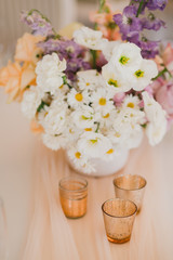 Coziness and style. Modern event design. Table setting at wedding reception. Floral compositions with beautiful flowers and greenery, candles, laying and plates on decorated table.