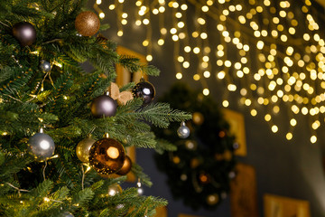 Obraz na płótnie Canvas Christmas and New Year interior - blur background: fireplace, lamps, green Christmas tree, brown leather sofa, gifts, candles, moose rocking chair. Lots of lights glowing in the dark.