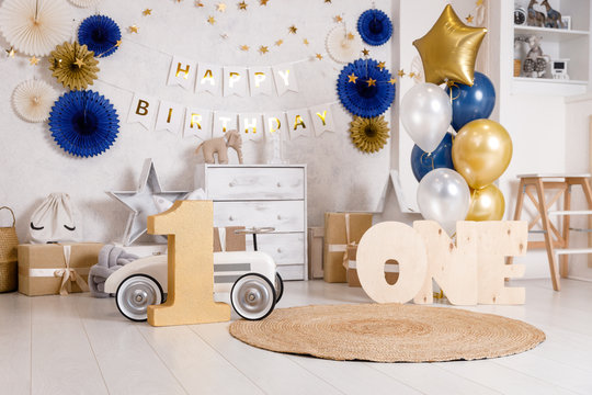 Birthday decorations with gifts, toys, balloons, garland and figure 1 for little baby party on a white wall background.