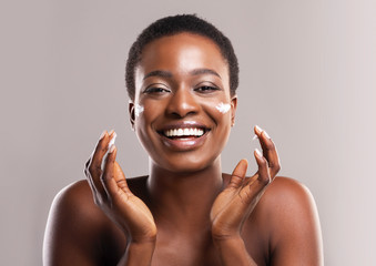 Portrait Of Joyful African Girl Applying Moisturizing Lotion on Face