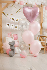 Birthday decorations with wooden arch, gifts, toys, balloons, garland and figure 3 for little baby party on a white wall background.