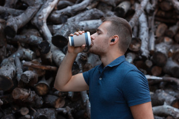 Young handsome man is drinking coffee and listening music with wireless headphones outside. Modern man with a bluetooth headset. Portrait