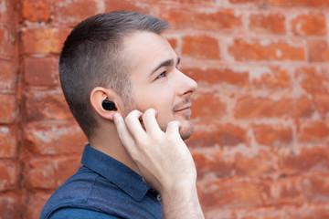 Young handsome man is listening music and pointing by finger on wireless earphone in his ear. Modern man with a bluetooth headphones. Close-up portrait.