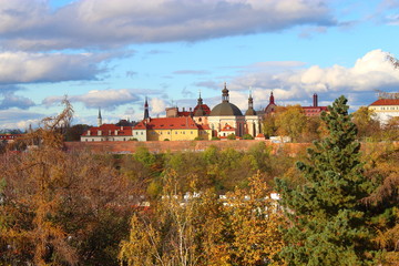 Naklejka premium View of the old buildings consisting of domes and spires against the blue sky and yellow-green trees in autumn in Prague.