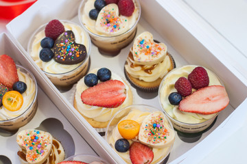 Cupcakes in cups with cream cheese frosting, fresh strawberries, blueberries, raspberries and chocolate sprinkled hearts. Gift box decorated with red ribbon. 
