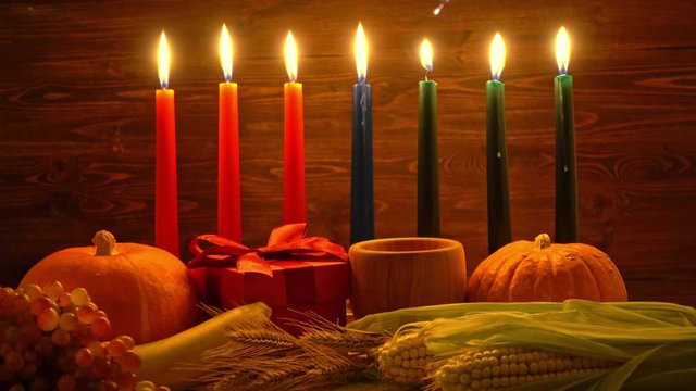 ignition of Kwanzaa traditional candles, festival concept with gift box, pumpkin, ears of wheat, grapes, corns, banana, bowl and fruits on wooden background