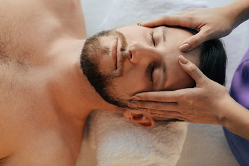 Fototapeta na wymiar Handsome man relaxing with eyes closed during head massage at wellness resort. Massage head pain treatment