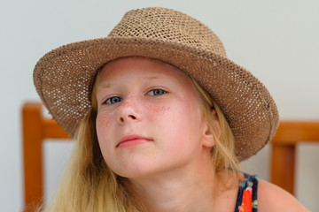 Beautiful tanned blonde girl with long hair in a brown straw hat sits on a chair, summer, portrait, smiling, emotion