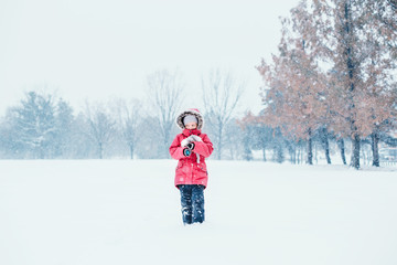 Fototapeta na wymiar Cute adorable sad unhappy abandoned Caucasian frozen girl child with toy standing alone in park during cold winter snowy day snowfall under falling snow. Kids outdoor seasonal activity.