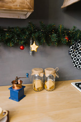 Two glass jars of cookies and a hand grinder on the table in the kitchen, decorated for Christmas