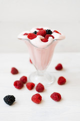 Milkshake with wild berries in a beautiful figured glass on a white wooden background. The concept of refreshing, cooling summer drinks. Selective focus
