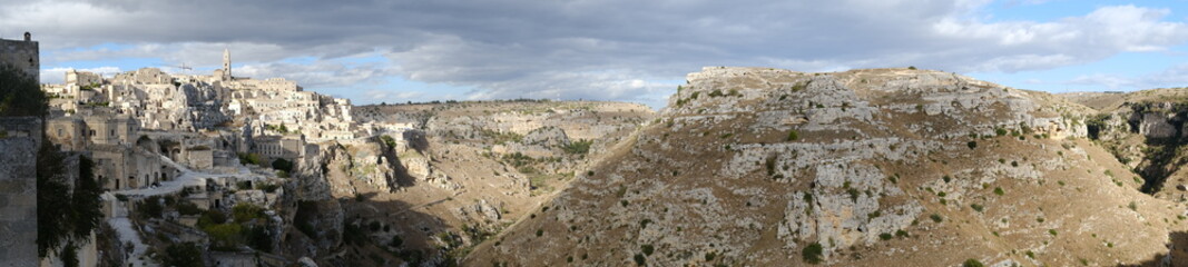 Fototapeta na wymiar Panoramic view of the Sassi of Matera with tuff stone houses. Mountains with sky and clouds.
