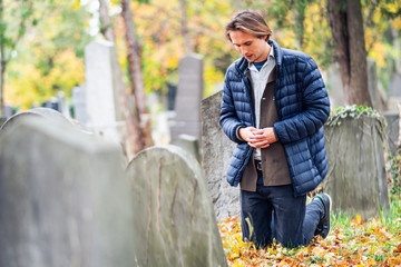 Mourning young man kneeling in front of a grave on a cemetery