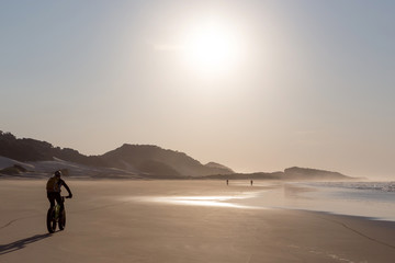 Cyclists riding into the sun along a deserted beach